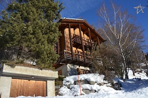 A wooden cabin with a balcony, surrounded by snow-covered ground and trees.