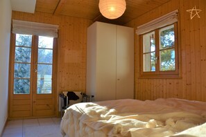 A bedroom with a bed, wooden walls, a wardrobe, and a window with a view of trees.