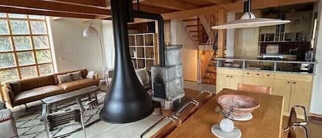 Ein gemütliches Interieur mit einem Holzesstisch, einem großen, schwarzen Herd und einer Couch.