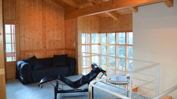 Ein Holzblockhaus-Interieur mit einem schwarzen Ledersessel, einer schwarzen Ledersofa und einem Stuhl mit Metallgestell.