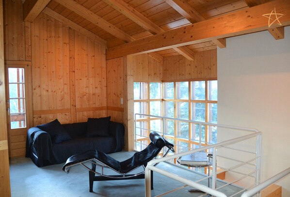 A wooden cabin interior with a black leather chair, a black leather sofa, and a metal-framed chair.