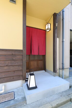 A wooden porch with a concrete step, a red cloth hanging, and a lantern on the step. - Kanazawa no yado Ikedaya (Kanazawa)