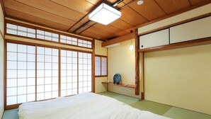 A traditional Japanese room with tatami flooring, a low wooden bed, sliding doors, and a shelf with a decorative item.