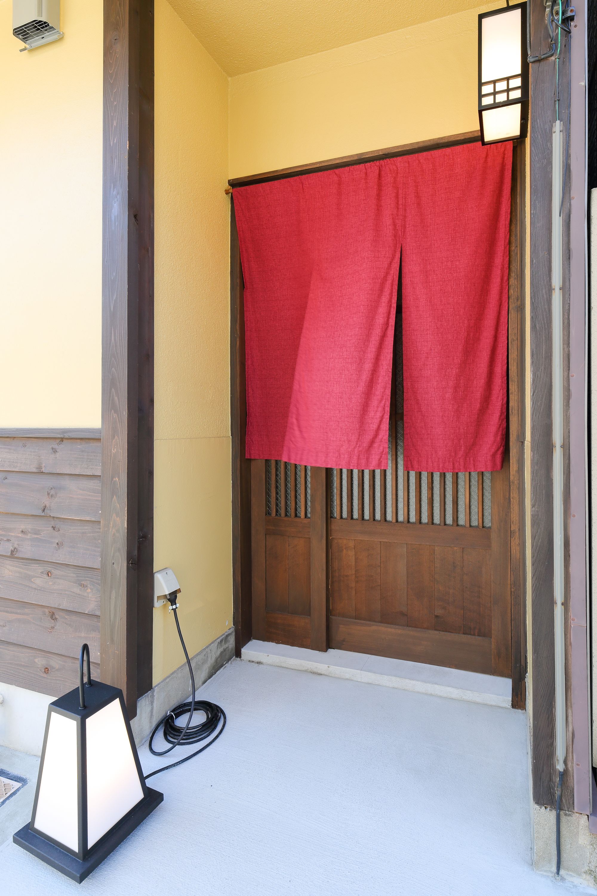 Una puerta de madera con una cortina roja, una luz exterior pequeña y un enchufe en la pared.