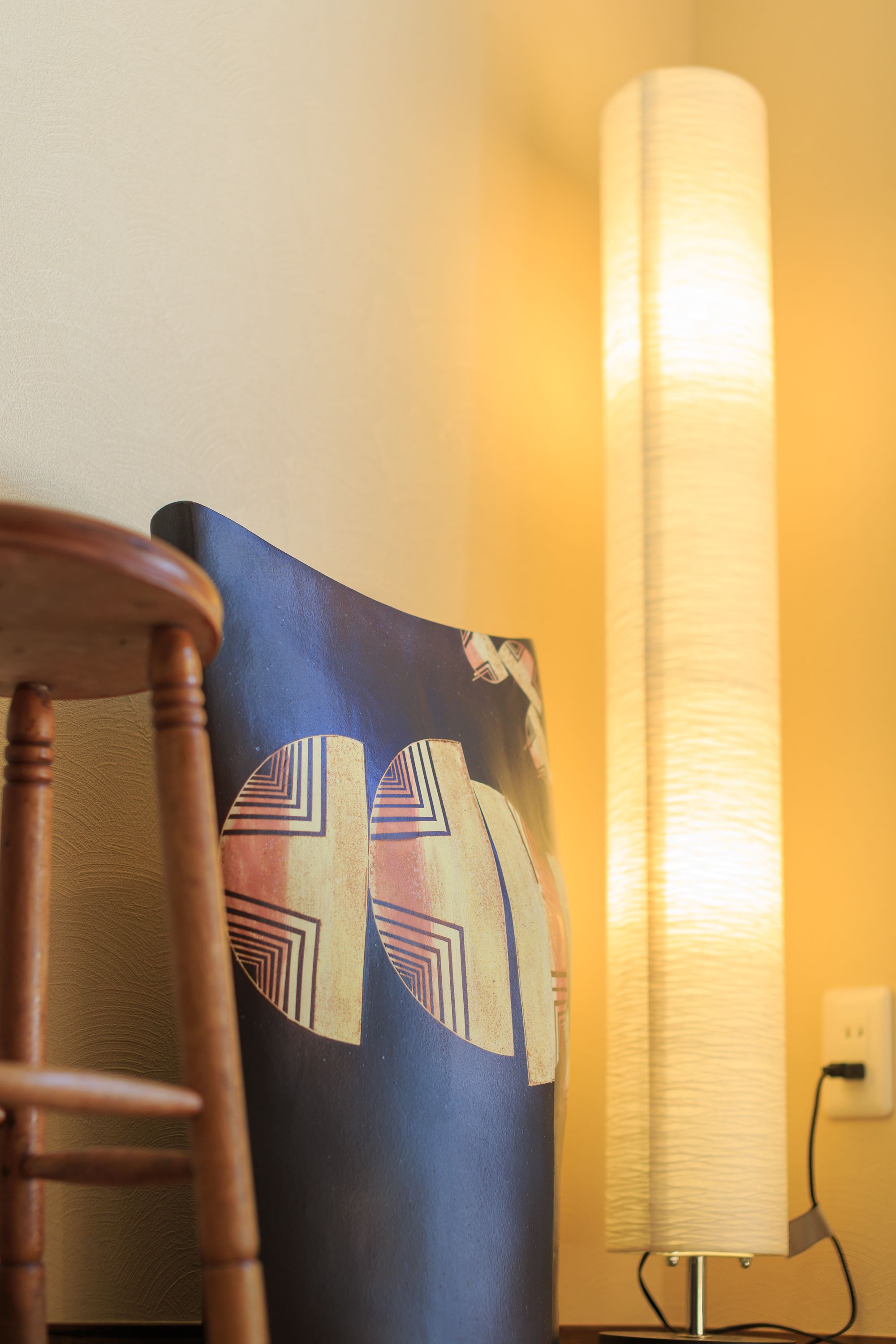 Een stoel en een wandlamp met een geometrisch patroon op een kussen.