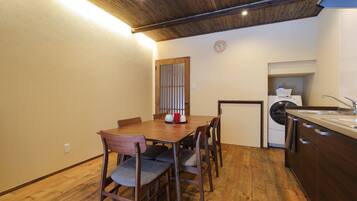A compact kitchen with wooden flooring, a dining table with chairs, a washing machine, and a clock on the wall.