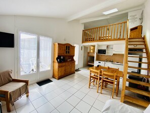 A compact living space with a dining area, kitchenette, and a loft bedroom with a wooden staircase. - Agréable pavillon dans résidence avec piscine (014) (Biscarrosse)