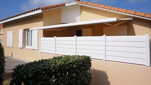 Una casa a un piano con facciata beige, tetto in tegole e recinzione bianca.