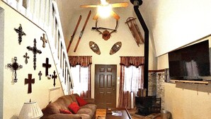 Una sala de estar con sofá, mesa de centro y chimenea. Se observan varias cruces en la pared y un televisor a la derecha.