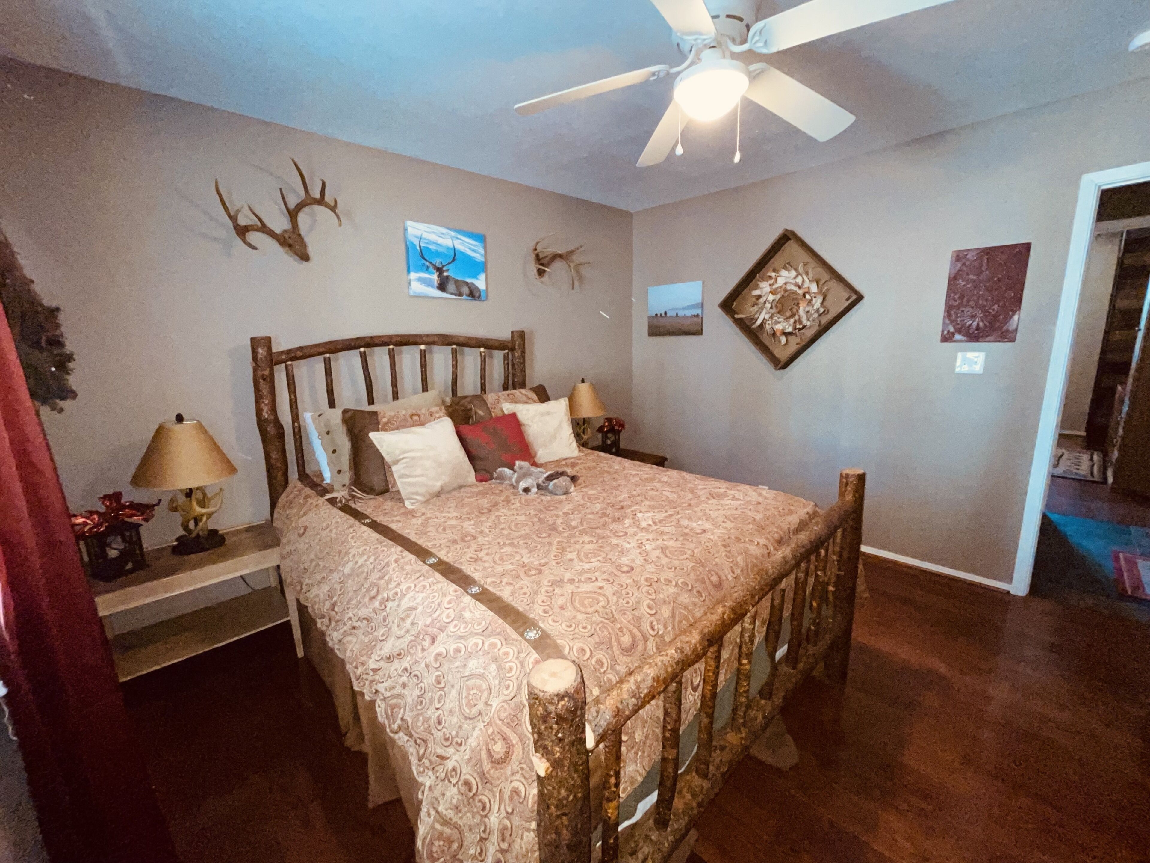 A bedroom with a wooden bed, a ceiling fan, and wall decorations including antlers and framed pictures.