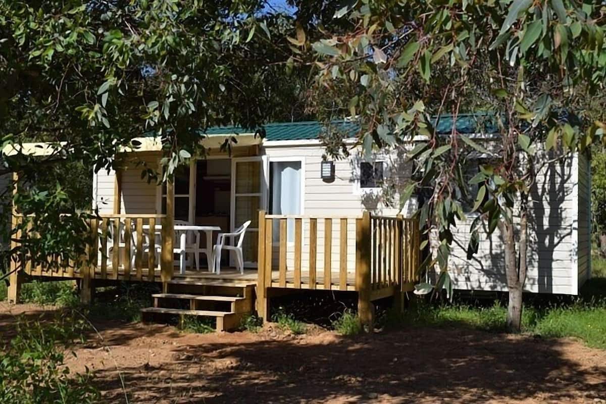 A small, single-story cabin with a wooden deck and a table with chairs.