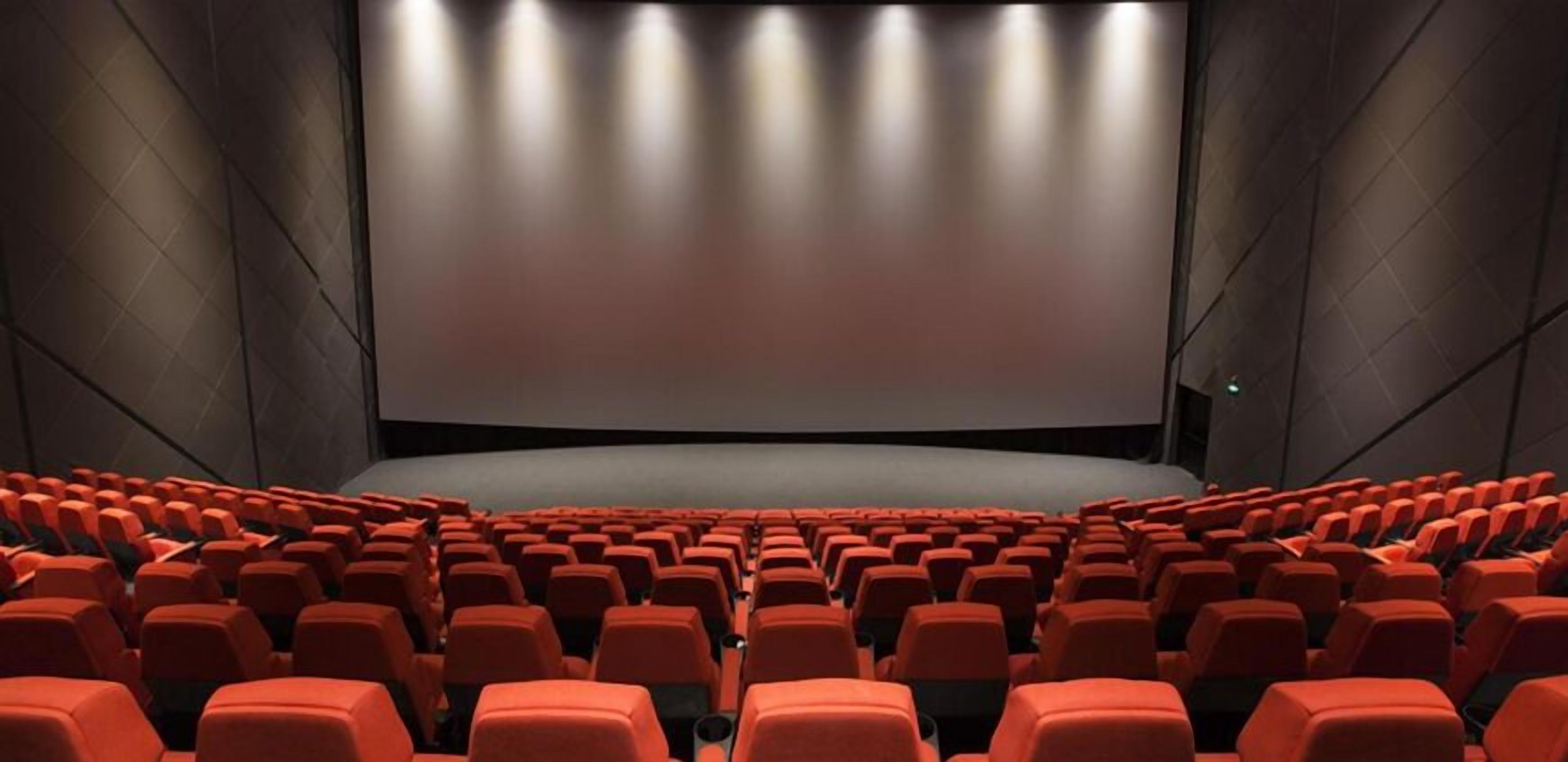 Un teatro con hileras de asientos rojos y una gran pantalla al frente.