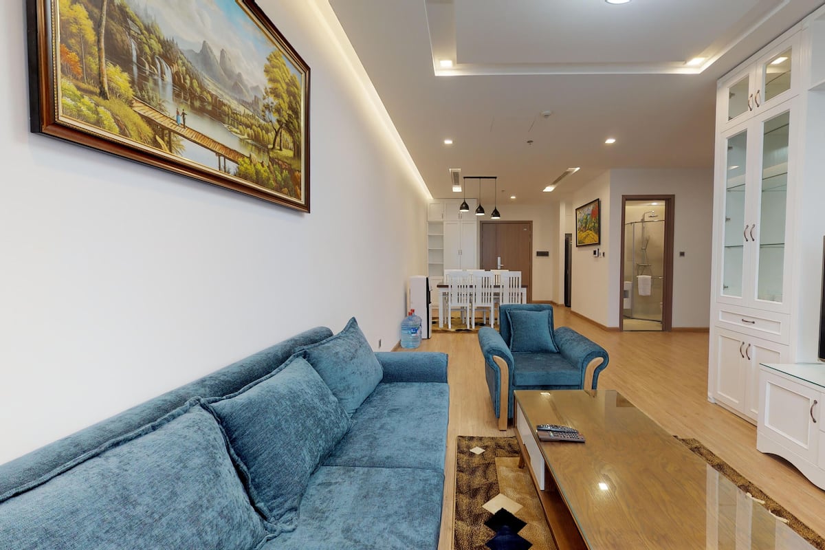 A modern living room with a sofa, armchairs, a TV, and a painting on the wall.