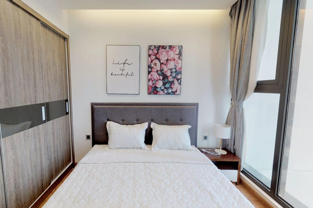A bedroom with a large wardrobe, a bed with white bedding, a headboard, and two framed pictures on the wall.