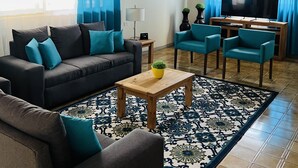 Una sala de estar con sofá, sillas, una mesa de centro, televisor y alfombra estampada.