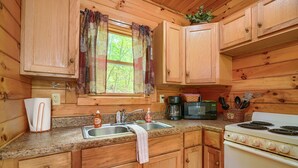 A wooden cabin kitchen with a sink, stove, and microwave. - Blue Rose Cabins - Big Woody Cabin (Logan)