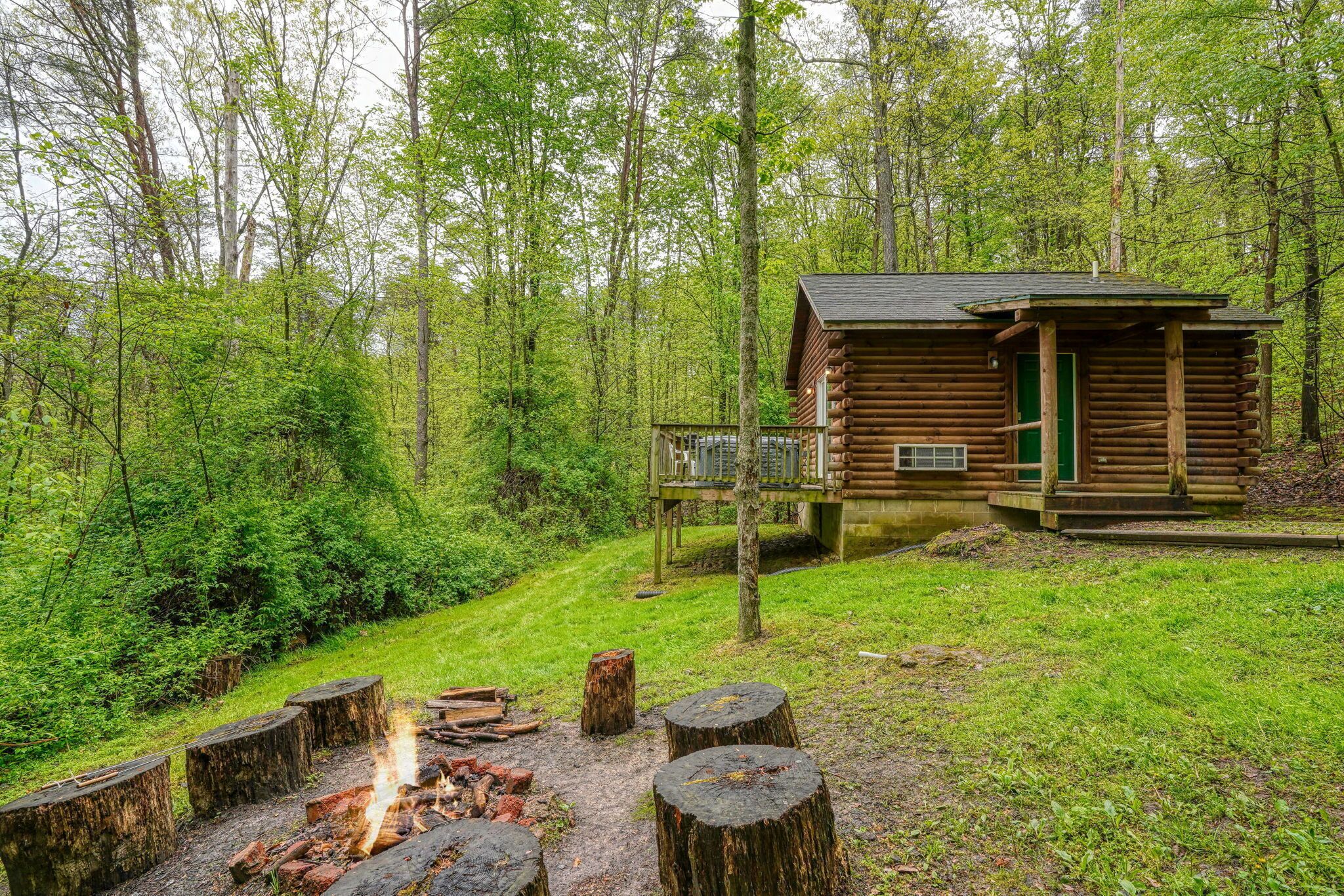 A rustic cabin with a deck, surrounded by a forest.