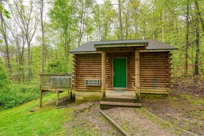 Una pequeña cabaña de madera con puerta verde, un porche y una terraza de madera.