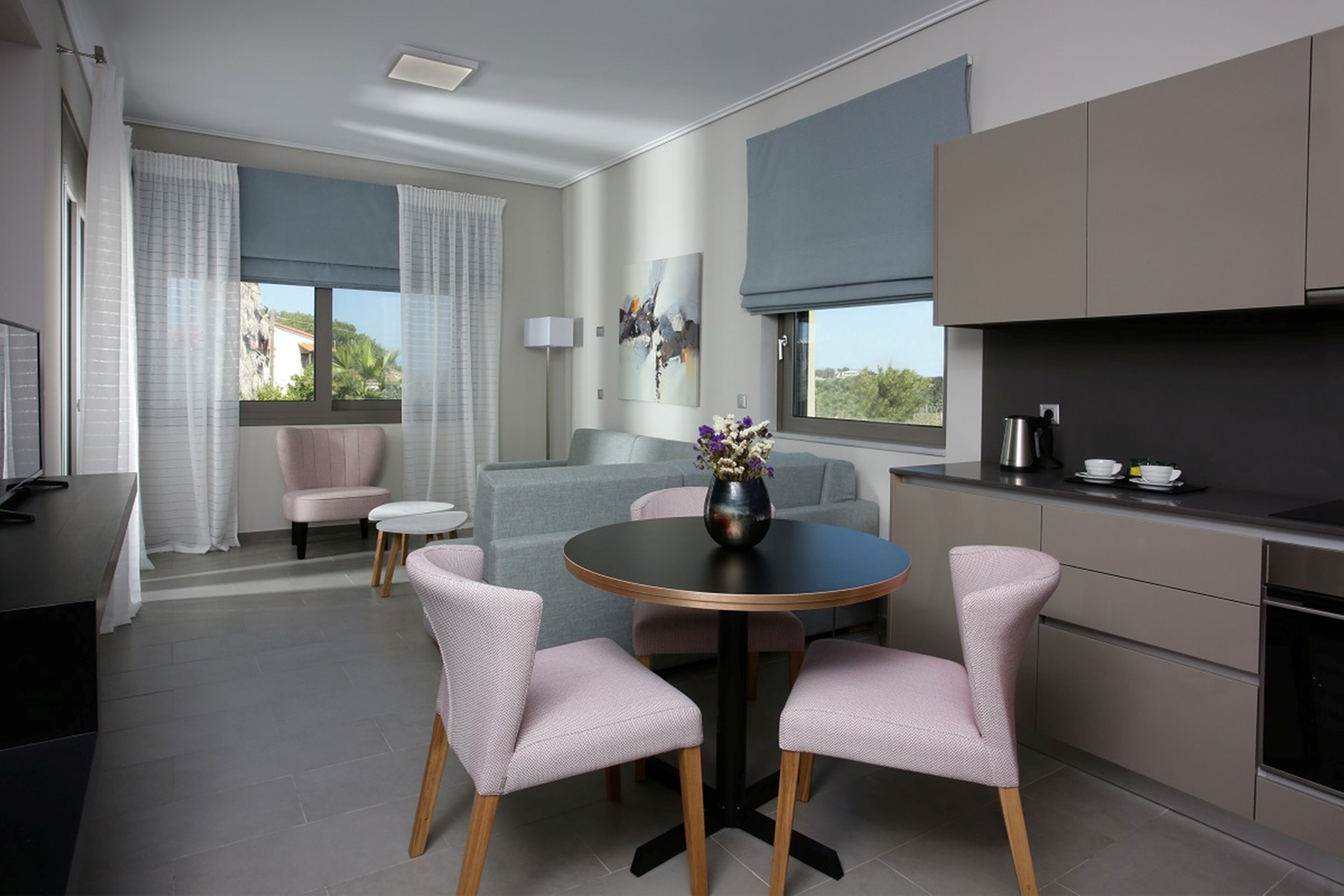 Una cucina moderna con mobili grigi, un tavolo rotondo con sedie rosa e una finestra con tende.