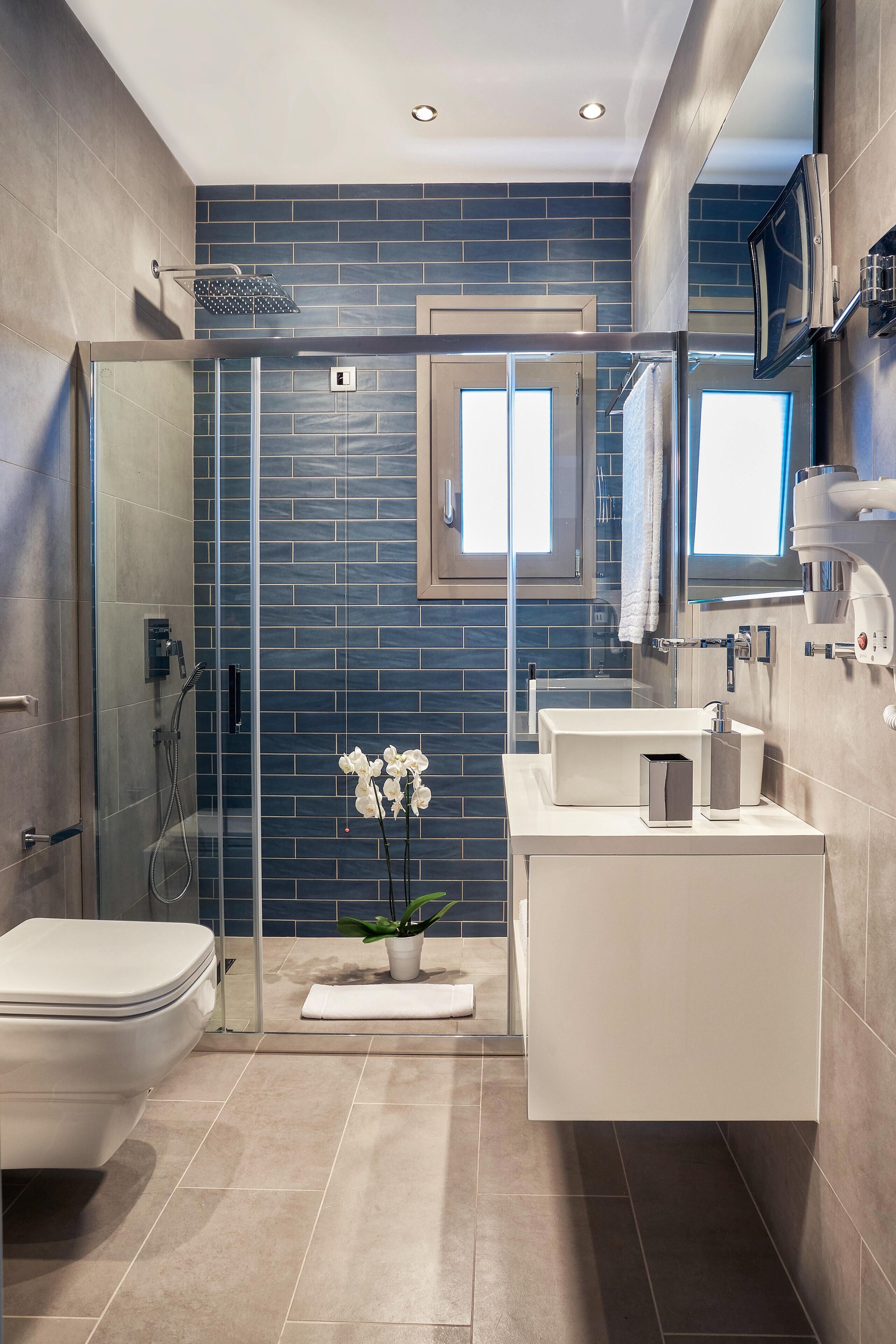 A modern bathroom with a glass shower enclosure, a white toilet, a sink with a mirror, and a potted orchid.