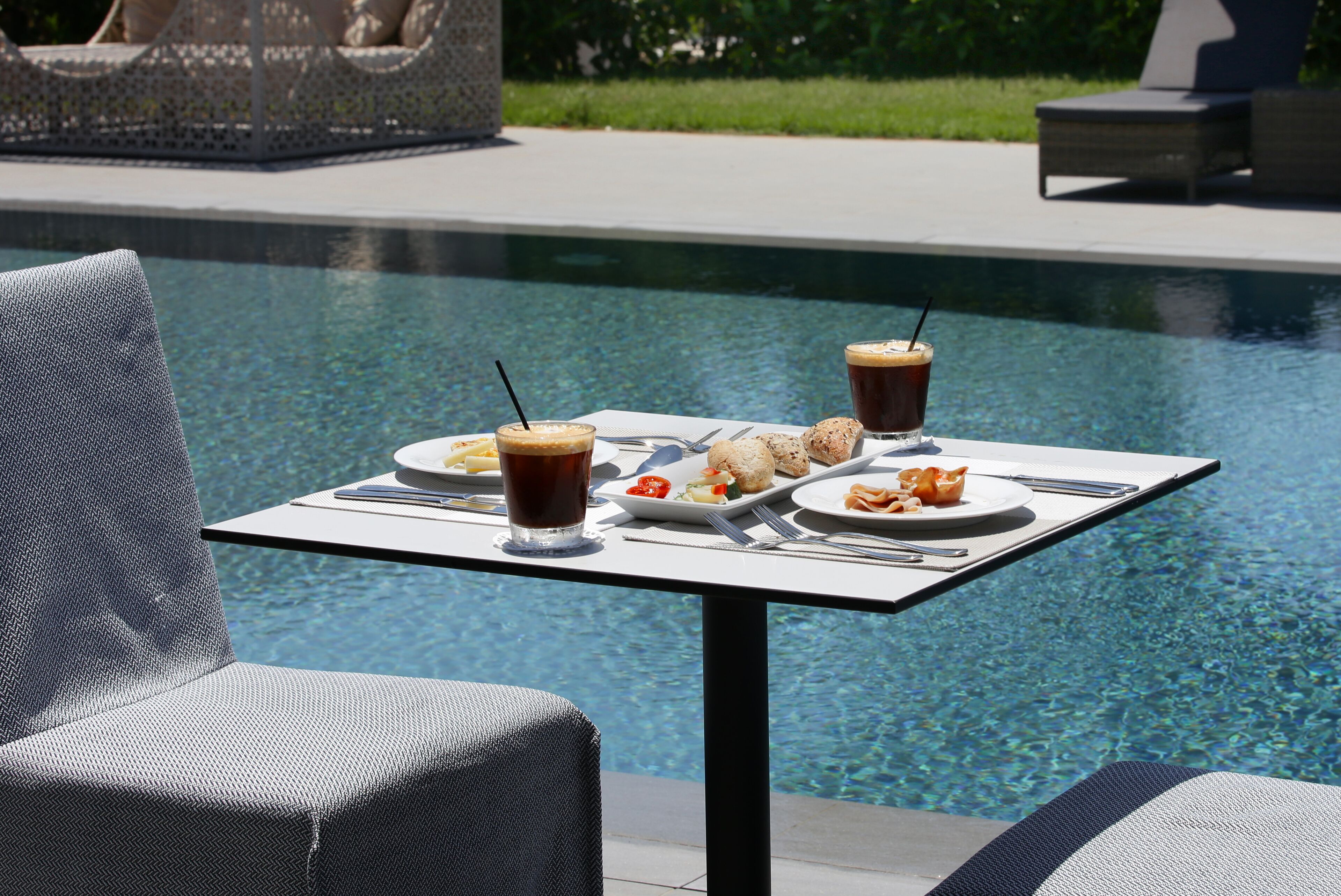 A dining table by a pool with food and drinks.