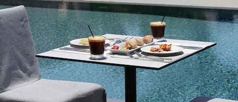 A dining table by a pool with food and drinks.