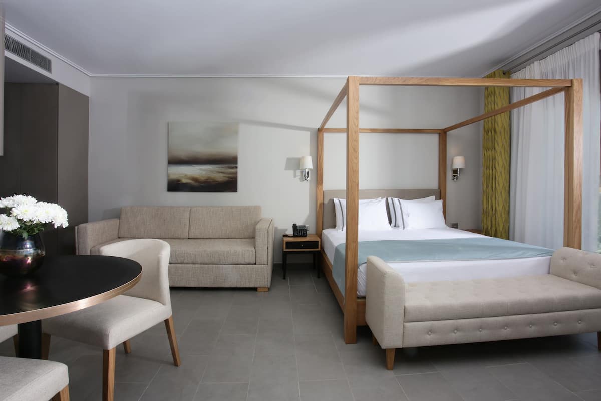 Ein modernes Hotelzimmer mit Himmelbett, einer Couch, einem Esstisch und einem Gemälde an der Wand.