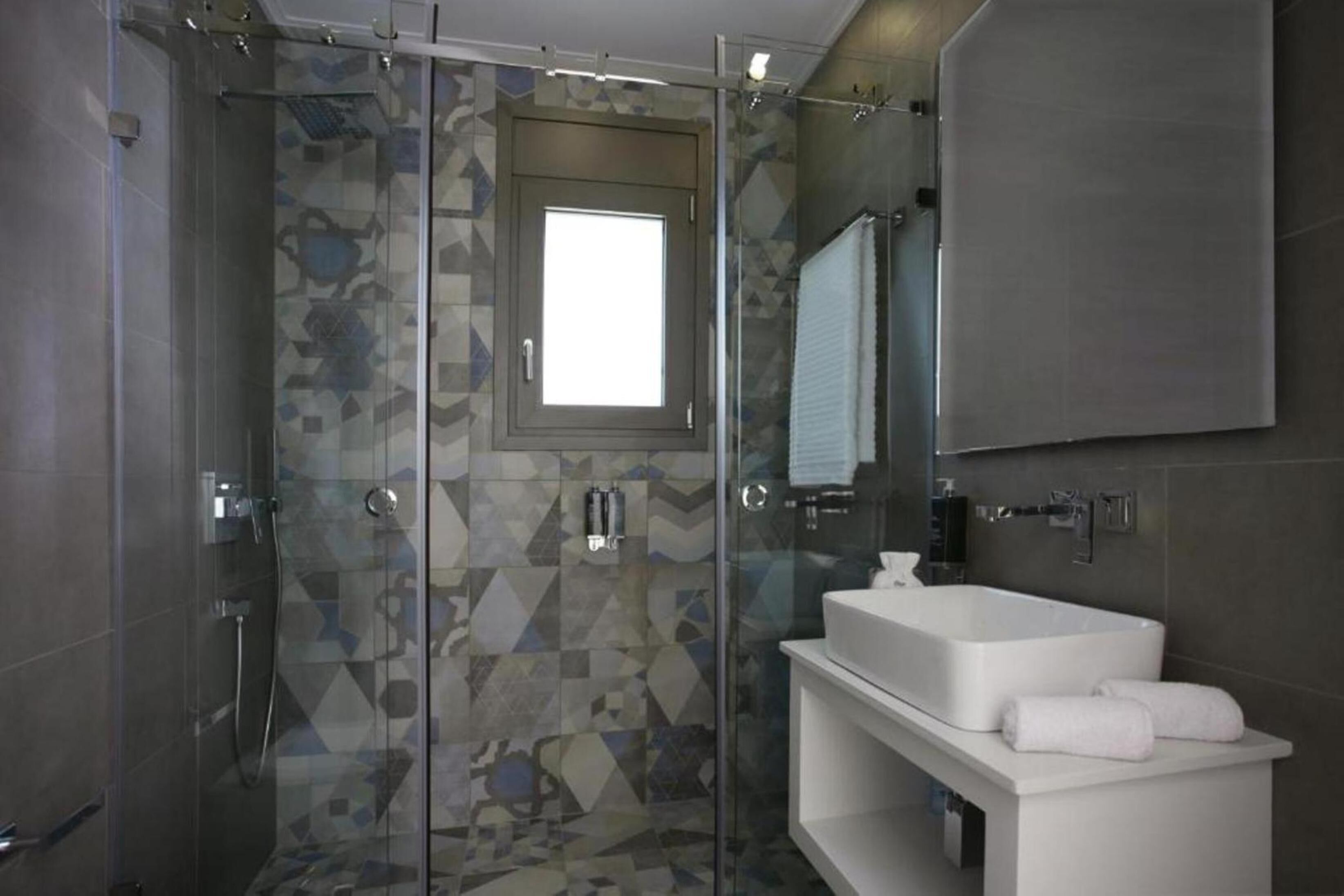 Een moderne badkamer met een douchecabine van glas, een witte wastafel en een grote spiegel.