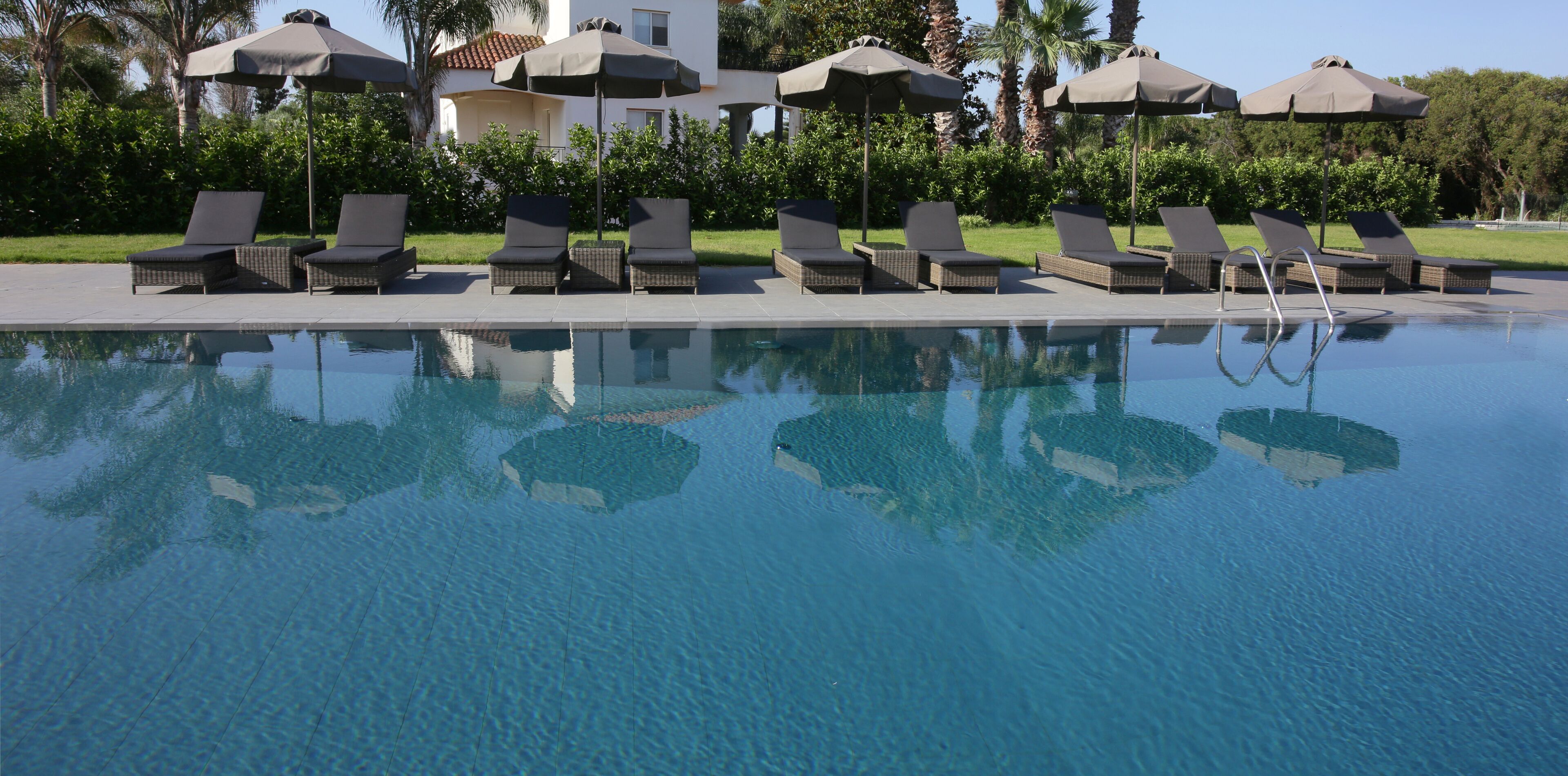A poolside area with lounge chairs and umbrellas, a clear pool, and a building in the background.