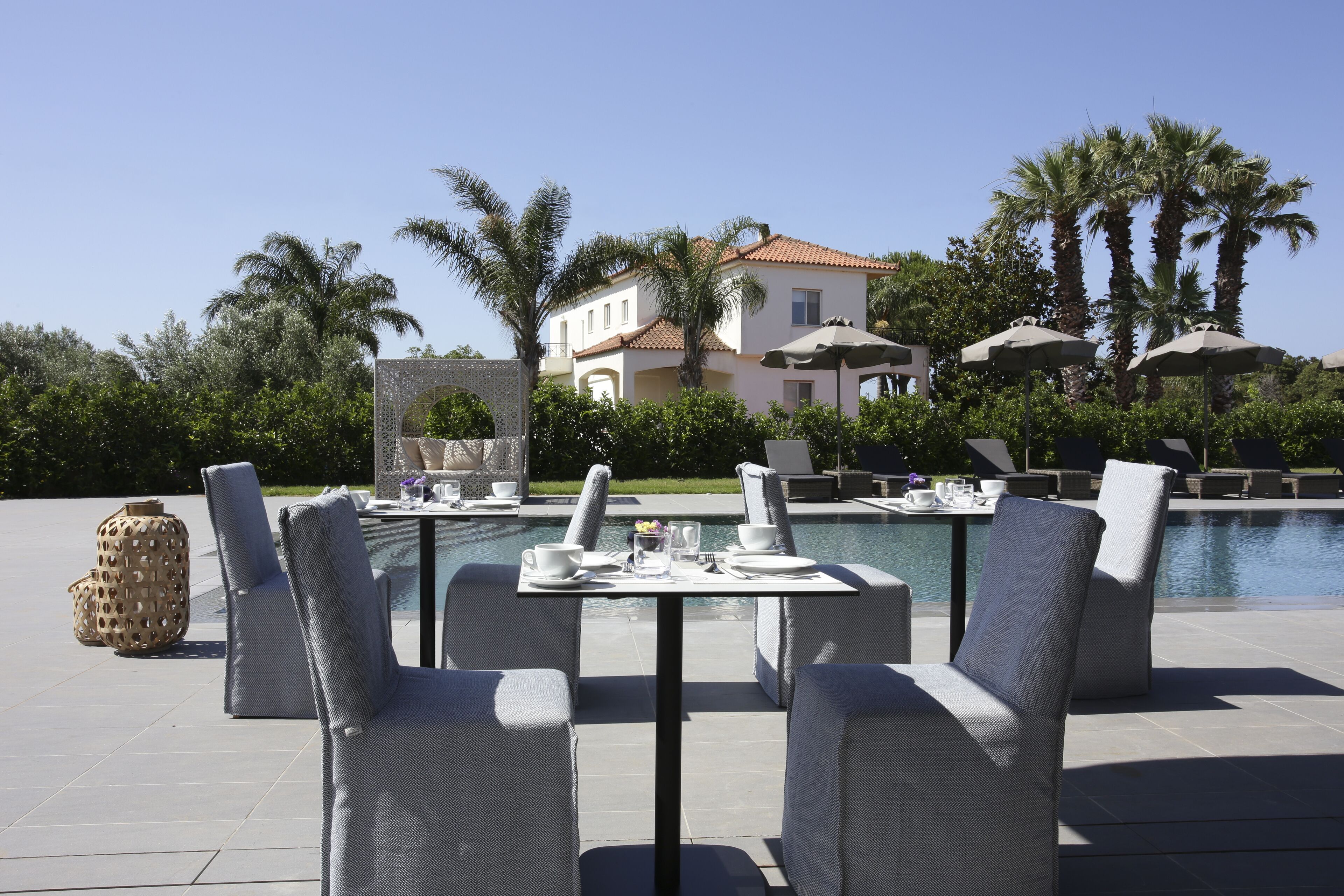 Un espace extérieur aménagé pour les repas, avec une piscine, des chaises longues et un bâtiment en arrière-plan.