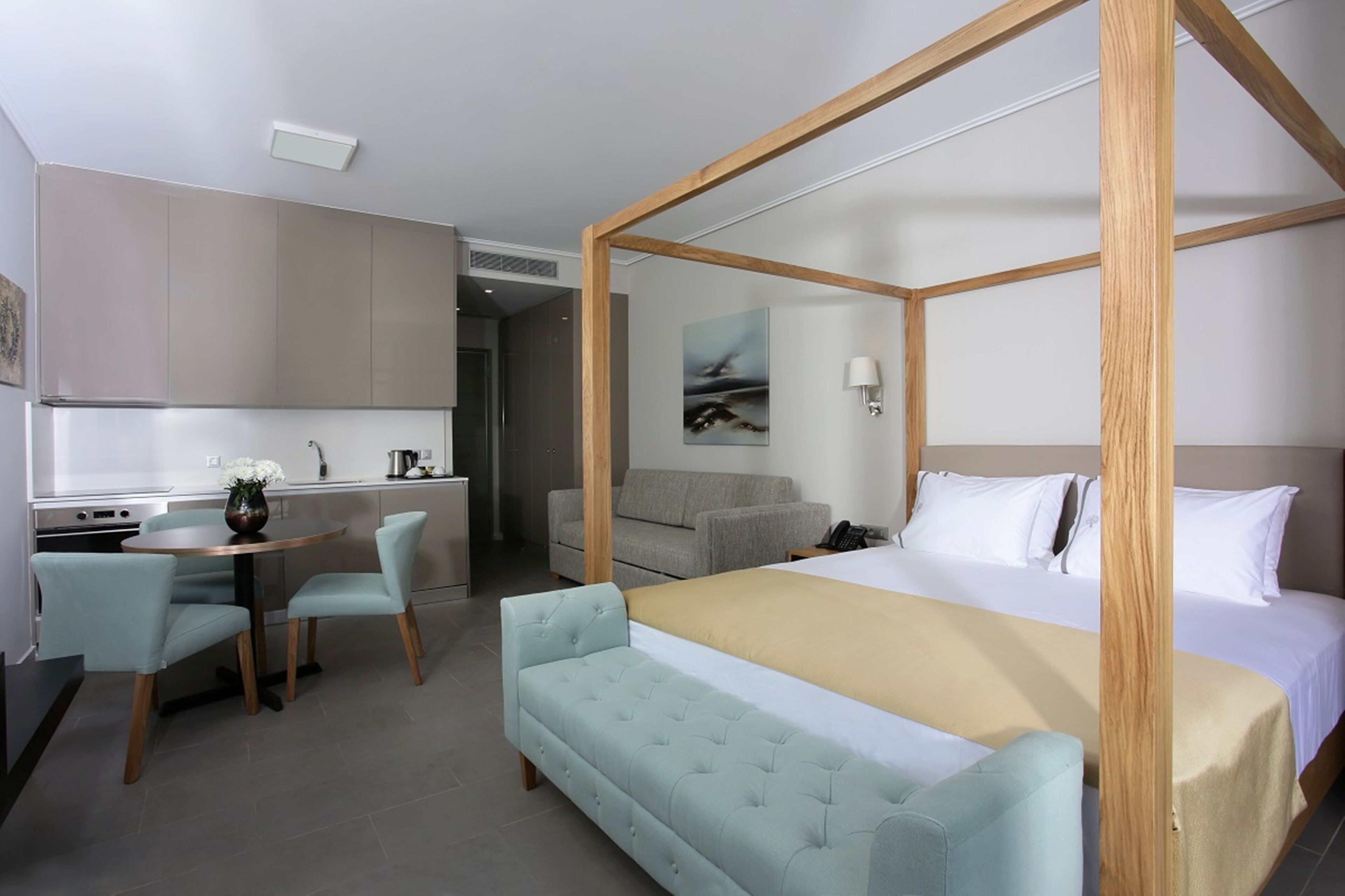 Una habitación de hotel moderna con una cama con dosel, una zona de comedor con una mesa redonda y sillas, y una kitchenette.