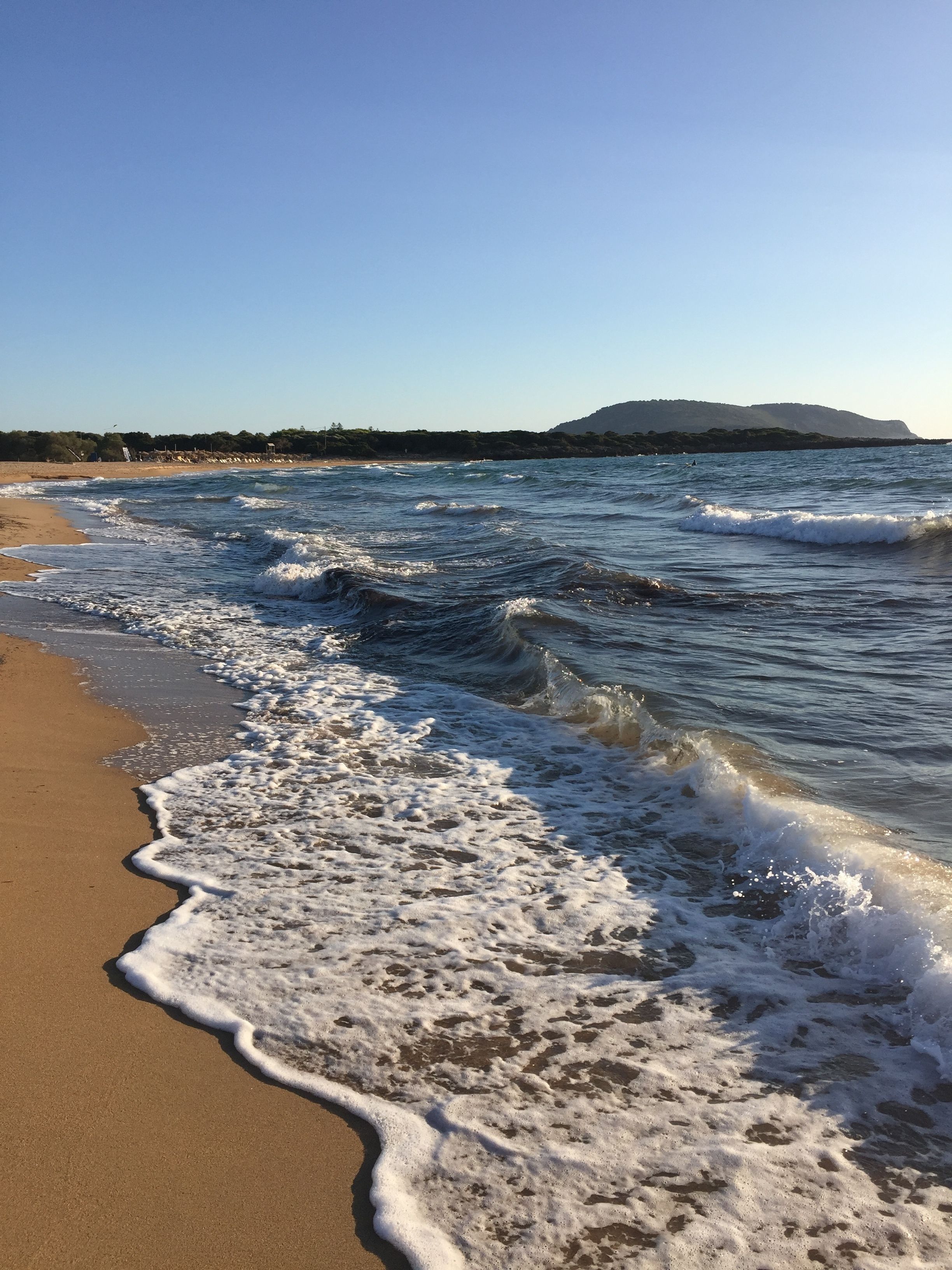 Ein Strand mit sanft anschwellenden Wellen, einem klaren Himmel und einer entfernten Hügelkette.
