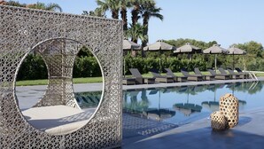 A poolside area with a decorative white lattice structure, lounge chairs, and umbrellas. - Hotel Lagouvardos Village (Trifylia)