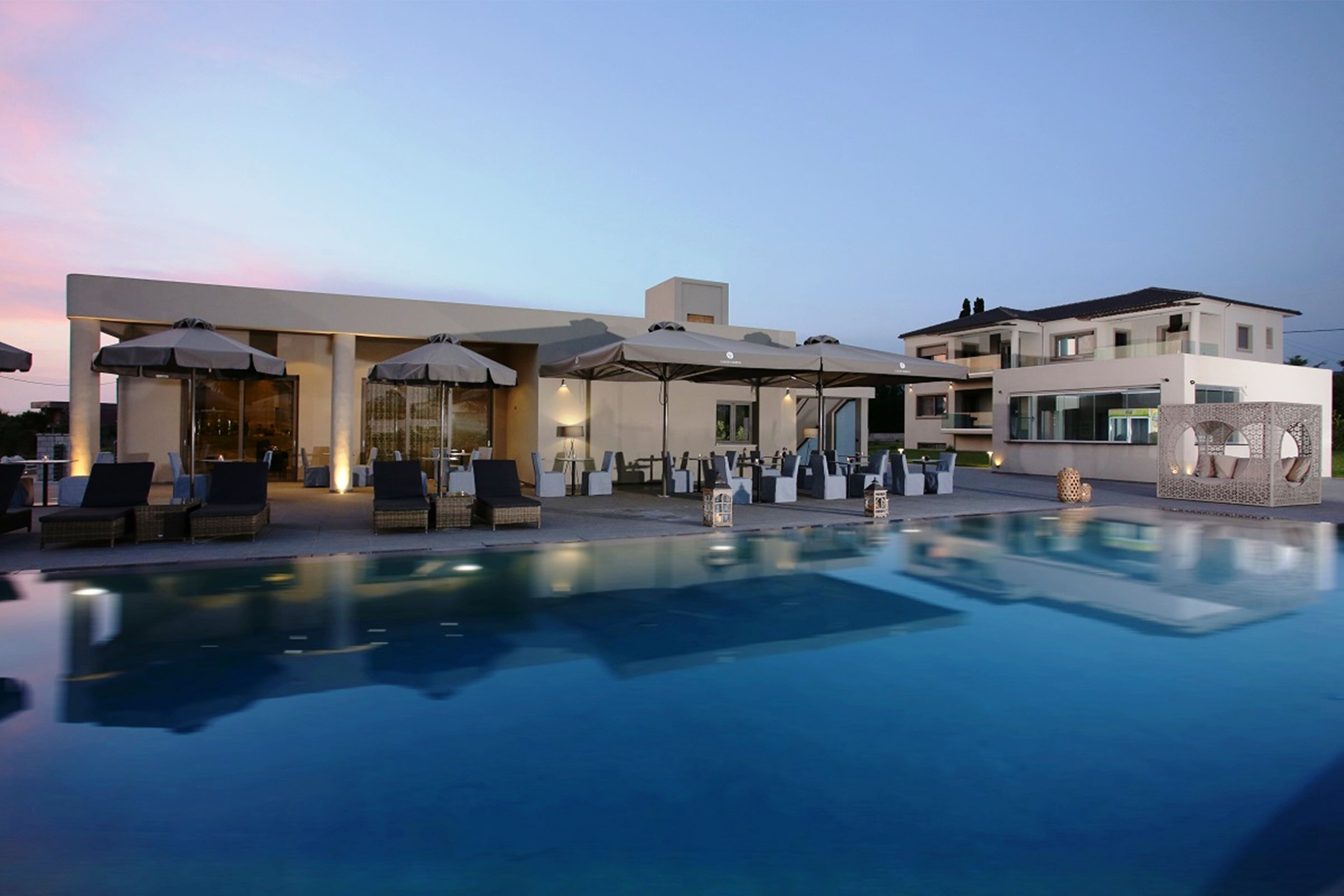 A modern hotel with a pool area, outdoor seating, and a well-lit facade.