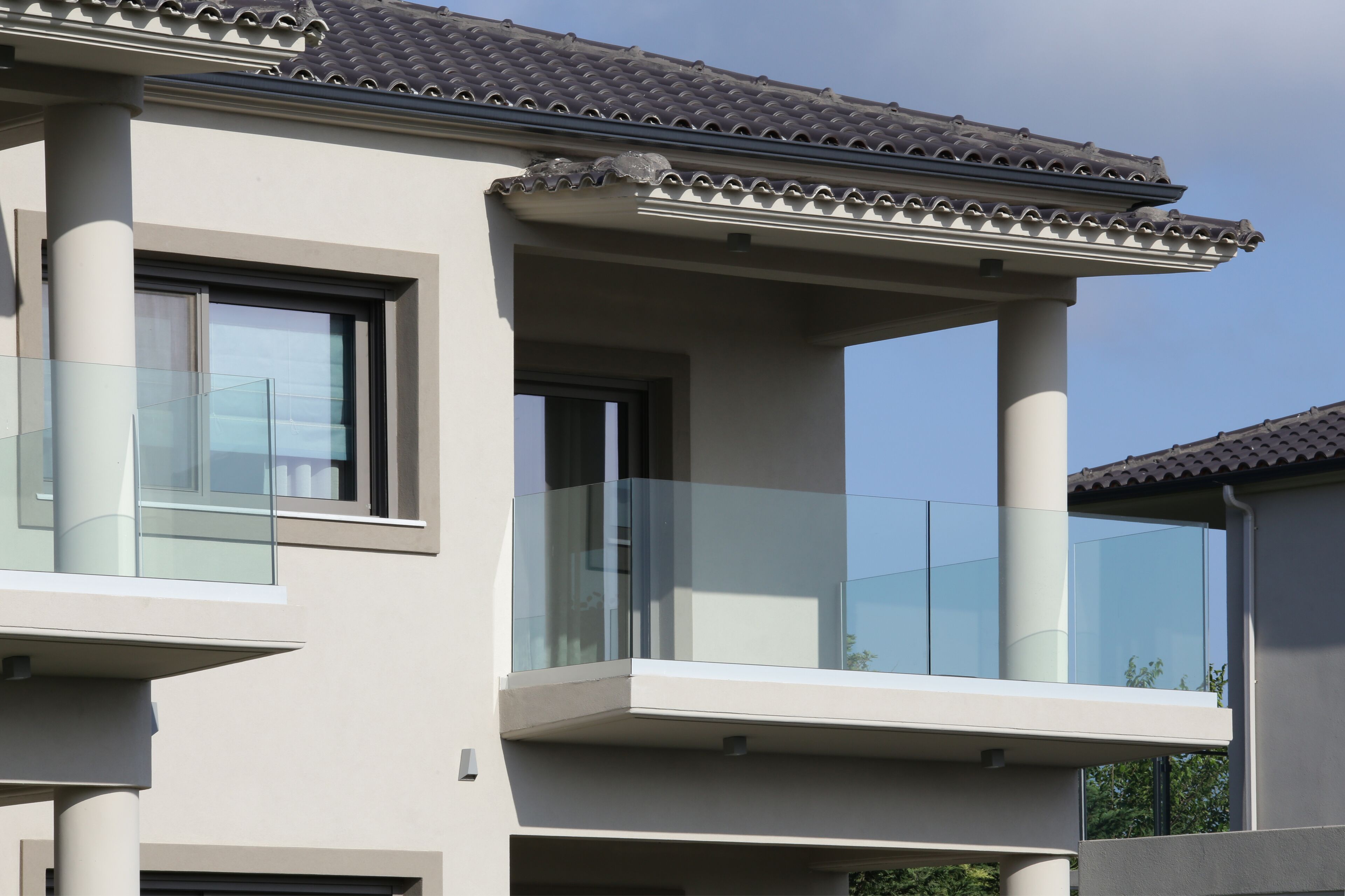 A modern building with a balcony, large windows, and a tiled roof.