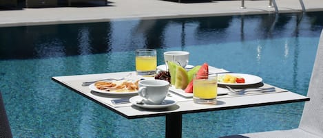 Una mesa de comedor con alimentos para el desayuno junto a una piscina.
