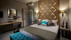 A modern hotel room with a large bed, a desk, a chair, and a bedside table with a lamp. - Hotel Lagouvardos Village (Trifylia)