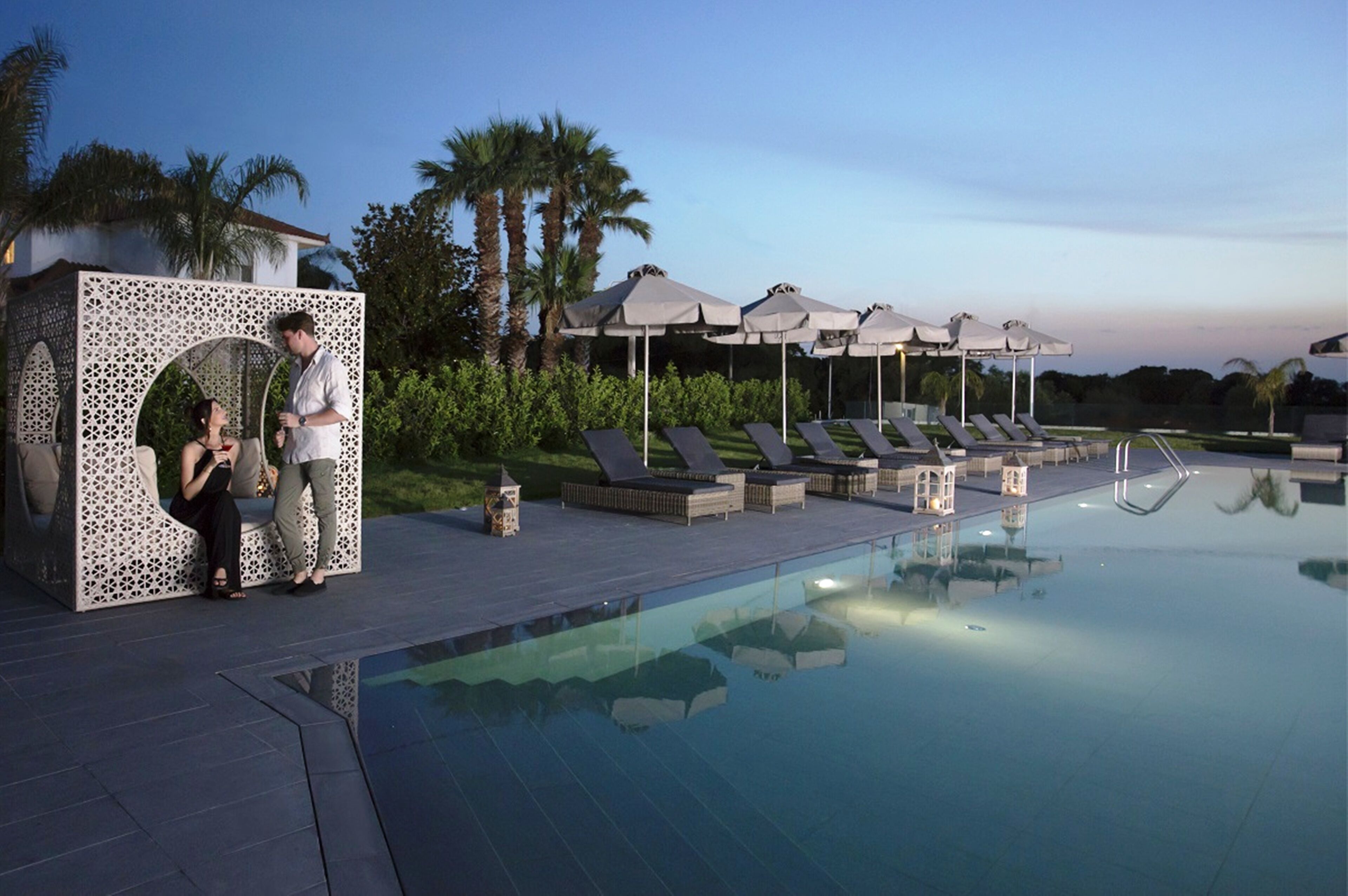 A poolside area with lounge chairs, umbrellas, and a decorative structure.