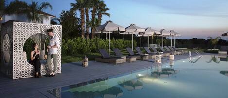 A poolside area with lounge chairs, umbrellas, and a decorative structure.