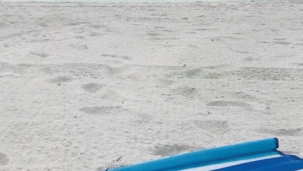 Eine Strandansicht mit einem blau gestreiften Handtuch und Flip-Flops im Sand.