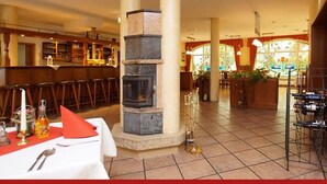 A restaurant with a bar area, a fireplace, and a dining table set with cutlery and a bottle. - Hotel & Restaurant zur Linde (Leuna)