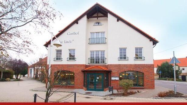 A two-story building with a white facade and red brick base. The building has a green door and multiple windows. - Hotel & Restaurant zur Linde (Leuna)