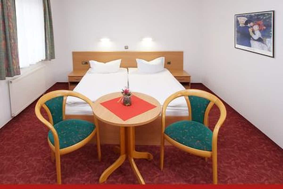 A hotel room with a bed, two chairs, a small table, and a painting on the wall.