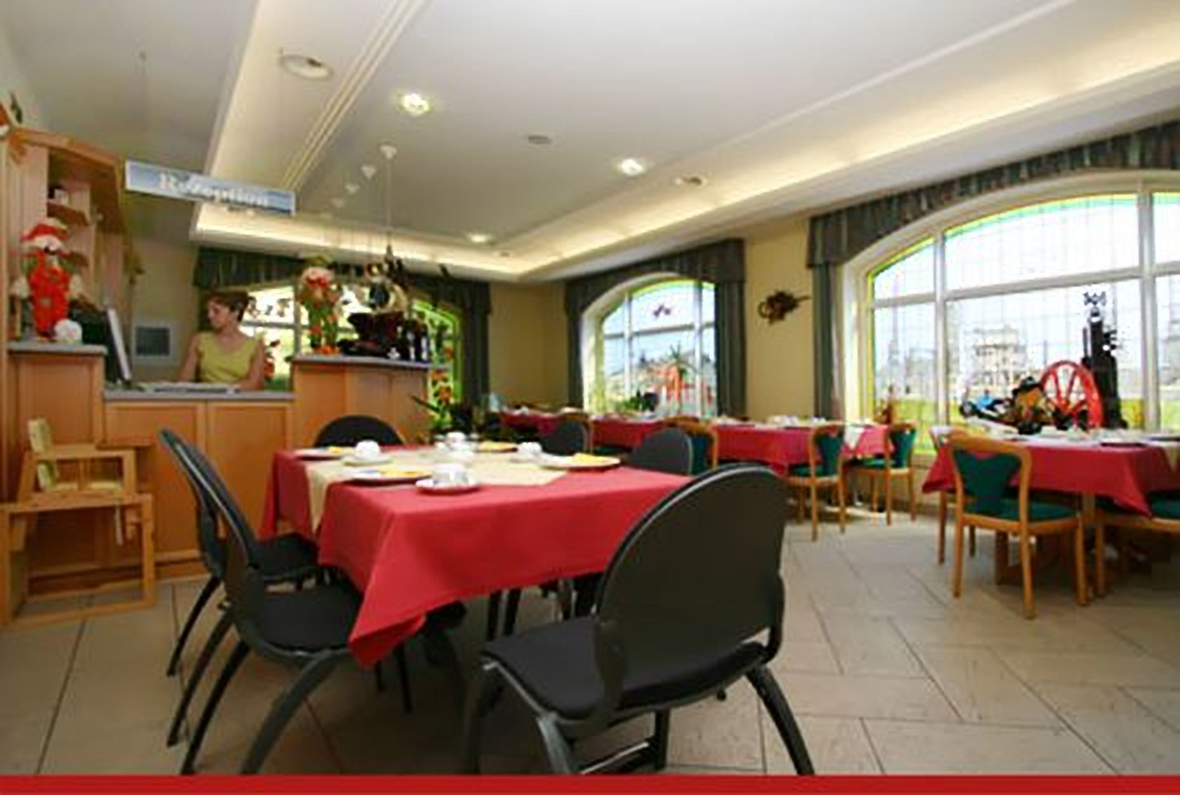 Un restaurante con varias mesas cubiertas de manteles rojos, sillas de madera y vistas a la ciudad a través de grandes ventanales.
