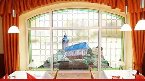 A room with a large window featuring a stained glass view of a building with a blue roof and a tower. - Hotel & Restaurant zur Linde (Leuna)