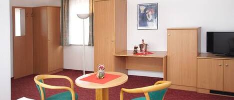 A hotel room with a wooden cabinet, a TV, a small table with chairs, and a painting on the wall.