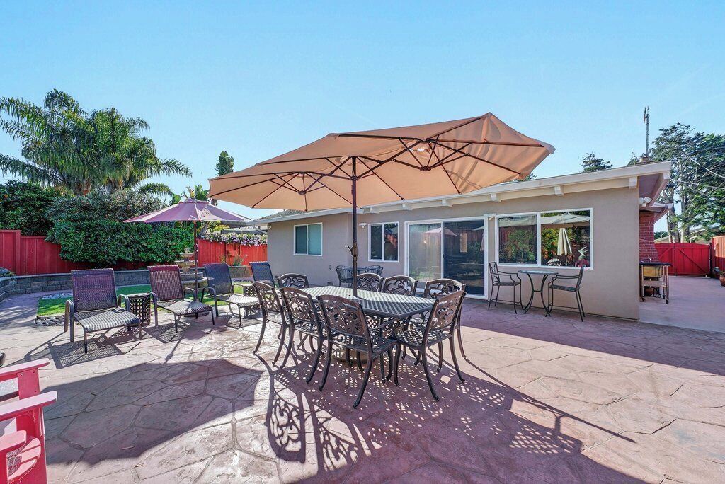 A patio with a table and chairs, a large umbrella, and a house in the background.