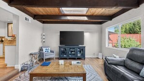 A living room with a wooden ceiling, a television, a grey sofa, and a black leather couch. - Spacious Open Floor Plan (Santa Cruz)