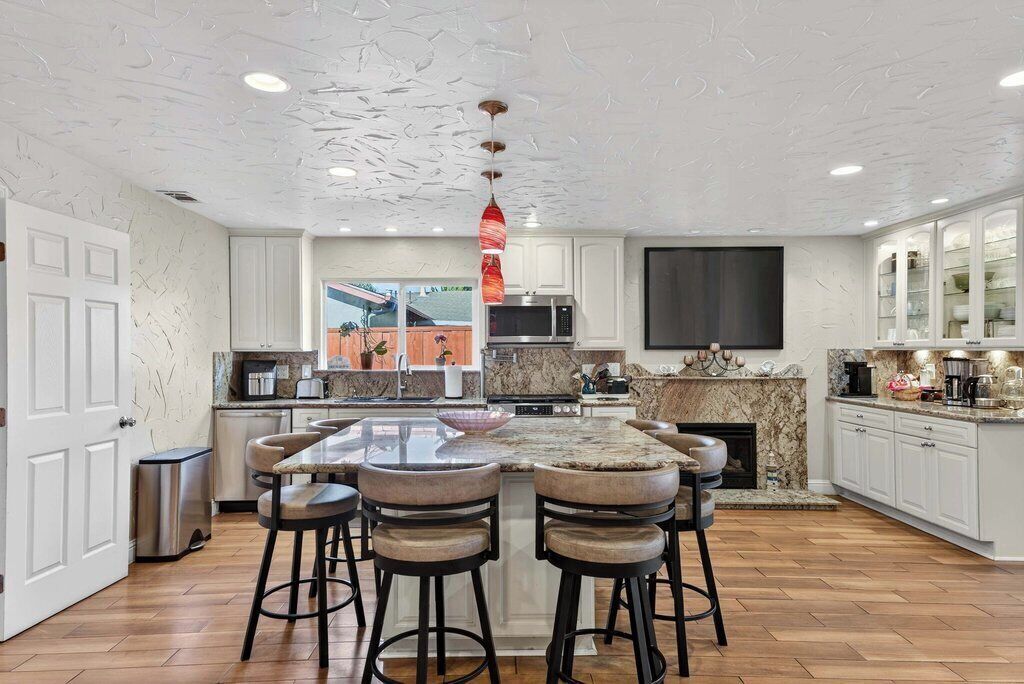 A modern kitchen with a central island, bar stools, a microwave, and a fireplace.
