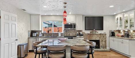 A modern kitchen with a central island, bar stools, a microwave, and a fireplace.